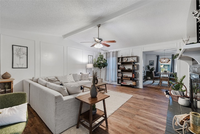 living room with hardwood / wood-style flooring, ceiling fan, vaulted ceiling with beams, and a textured ceiling