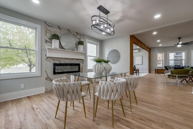 dining room featuring plenty of natural light, a premium fireplace, ceiling fan with notable chandelier, and light hardwood / wood-style flooring