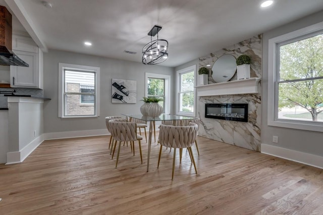 dining area with a premium fireplace, a notable chandelier, and light hardwood / wood-style flooring