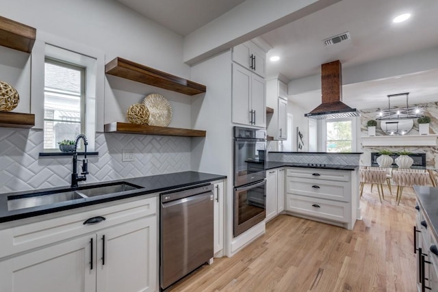 kitchen featuring sink, white cabinetry, multiple ovens, island range hood, and stainless steel dishwasher