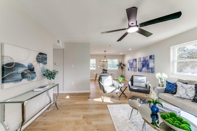 living room with ceiling fan with notable chandelier and light hardwood / wood-style floors