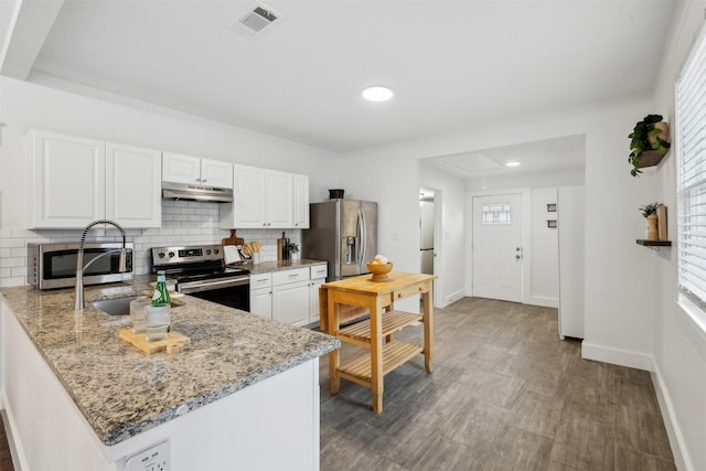 kitchen with appliances with stainless steel finishes, light stone counters, white cabinets, decorative backsplash, and kitchen peninsula