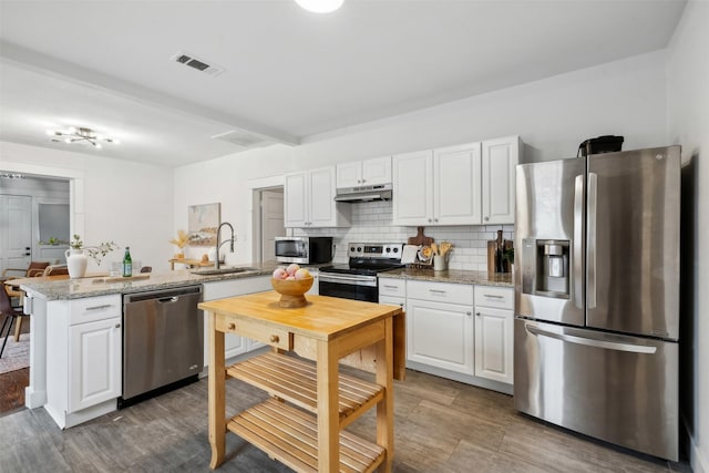 kitchen with white cabinetry, stainless steel appliances, light stone counters, and backsplash