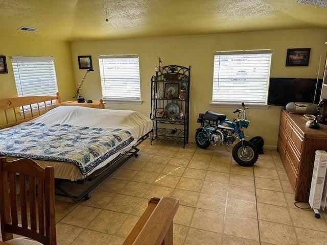 bedroom with multiple windows, a textured ceiling, and light tile patterned flooring