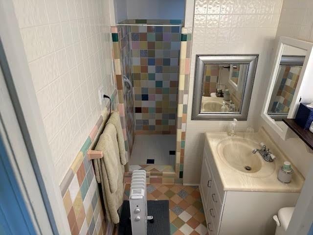 bathroom with vanity, tiled shower, and tile walls