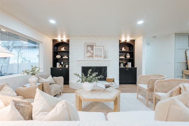 living room with built in shelves, a fireplace, and light hardwood / wood-style flooring