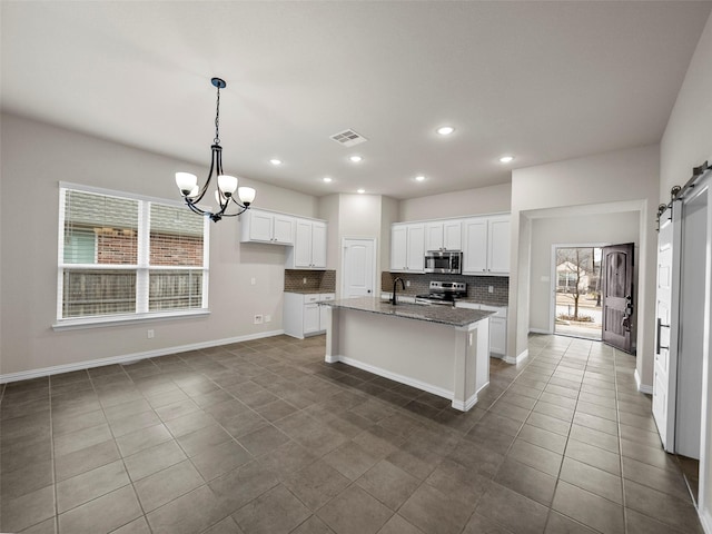 kitchen with white cabinetry, stainless steel appliances, a barn door, and a center island with sink