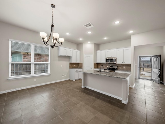 kitchen featuring stone counters, a center island with sink, white cabinets, and appliances with stainless steel finishes