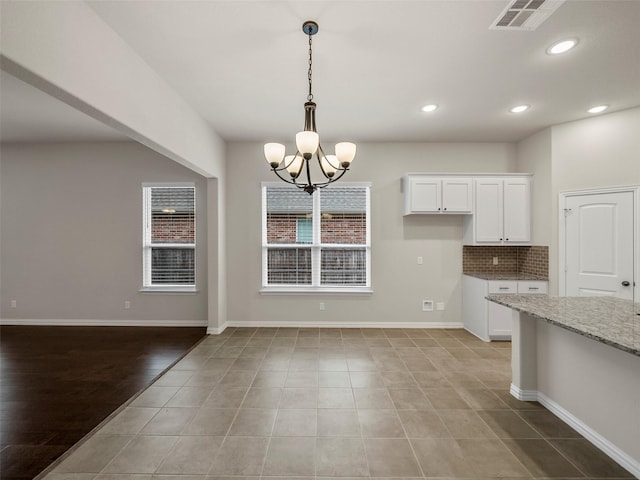 kitchen with tasteful backsplash, white cabinets, hanging light fixtures, light stone countertops, and an inviting chandelier