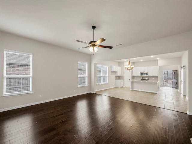 unfurnished living room with ceiling fan with notable chandelier, light hardwood / wood-style flooring, and a wealth of natural light