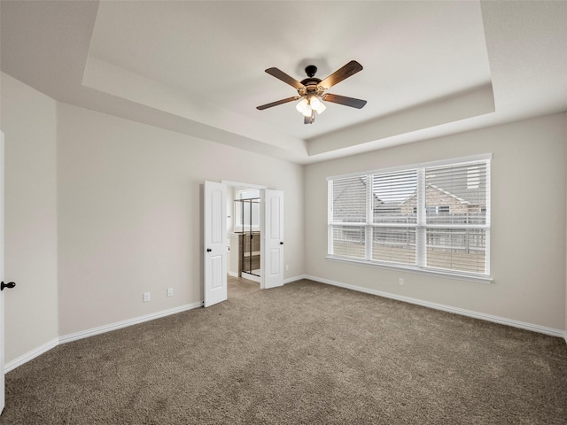 unfurnished bedroom with ceiling fan, ensuite bath, a raised ceiling, and dark colored carpet