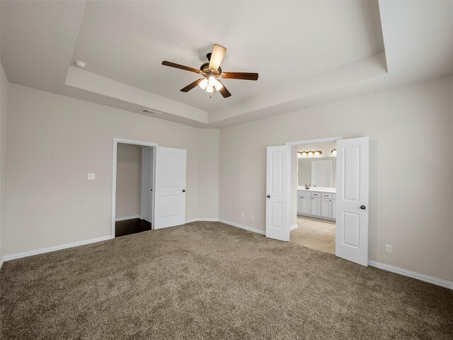 unfurnished bedroom featuring ceiling fan, light colored carpet, ensuite bathroom, and a raised ceiling