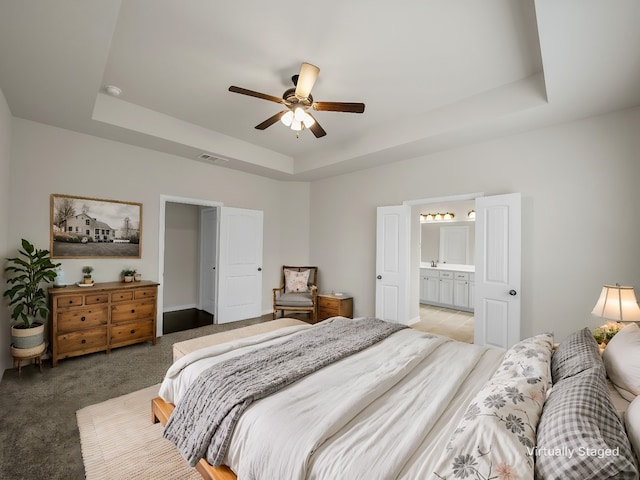 bedroom featuring ceiling fan, connected bathroom, a tray ceiling, and light carpet