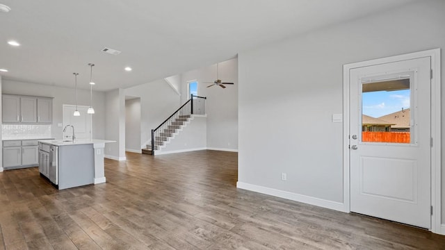 kitchen featuring dark wood-type flooring, sink, decorative light fixtures, a center island with sink, and decorative backsplash