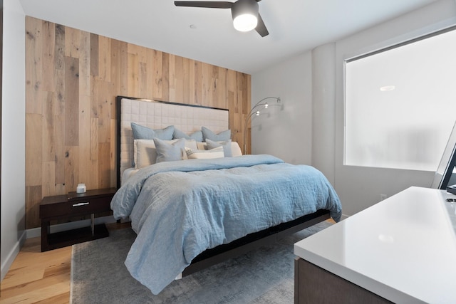 bedroom with wooden walls, ceiling fan, and light wood-type flooring