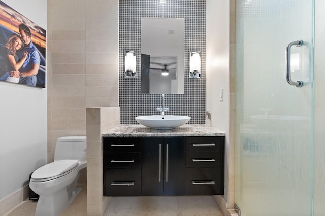 bathroom with toilet, tile walls, vanity, a shower with door, and decorative backsplash