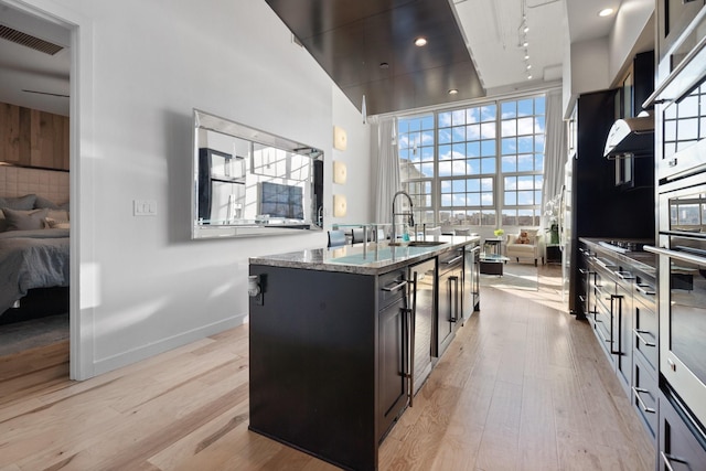 kitchen with extractor fan, sink, an island with sink, light stone countertops, and light hardwood / wood-style floors