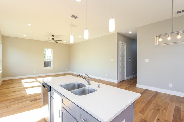 kitchen with sink, decorative light fixtures, light hardwood / wood-style flooring, dishwasher, and an island with sink