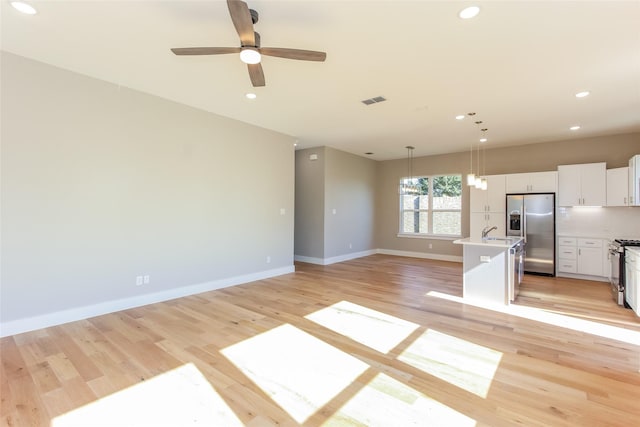 kitchen featuring white cabinetry, hanging light fixtures, a kitchen island with sink, stainless steel appliances, and light hardwood / wood-style flooring