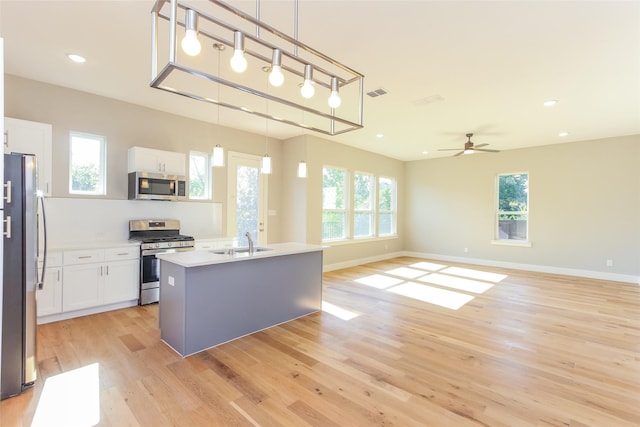 kitchen featuring decorative light fixtures, sink, white cabinets, stainless steel appliances, and a center island with sink