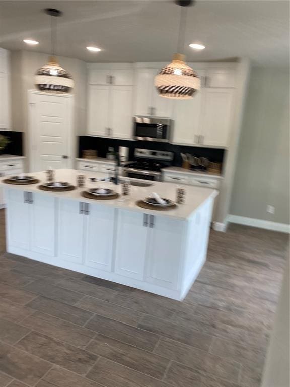 kitchen featuring stainless steel appliances, an island with sink, hanging light fixtures, and white cabinets