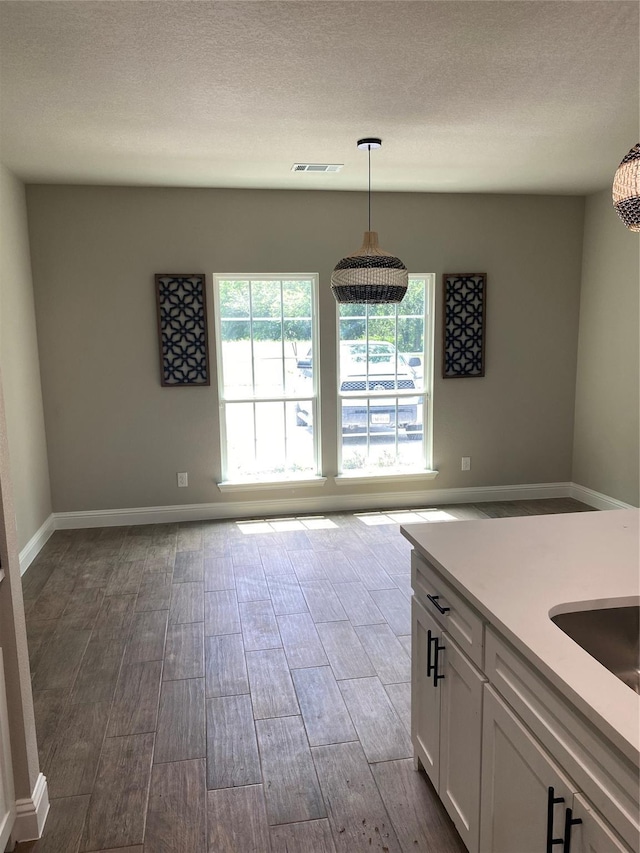 kitchen featuring pendant lighting, white cabinets, a textured ceiling, and light hardwood / wood-style flooring