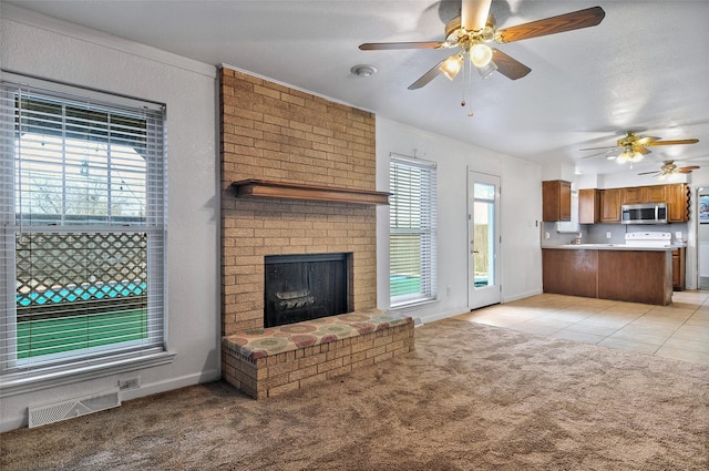 unfurnished living room with a brick fireplace, ornamental molding, light colored carpet, and ceiling fan