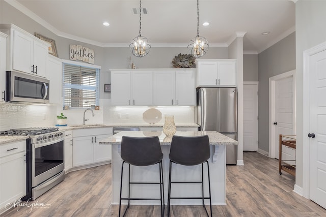 kitchen with sink, appliances with stainless steel finishes, light stone counters, white cabinets, and a kitchen island