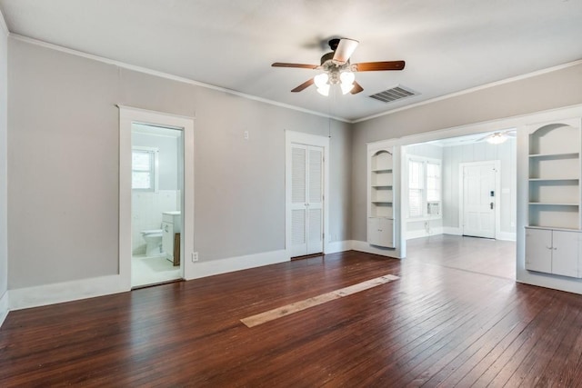 spare room with built in shelves, dark wood-type flooring, ornamental molding, and ceiling fan