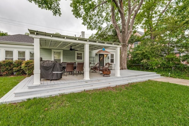 rear view of house featuring ceiling fan, an outdoor fire pit, a deck, and a lawn