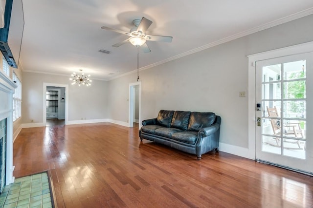 living room with wood-type flooring, crown molding, ceiling fan with notable chandelier, and a fireplace