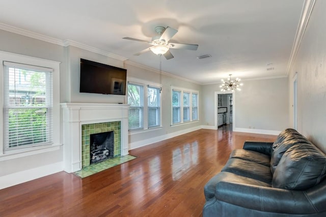 living room featuring ceiling fan with notable chandelier, wood-type flooring, ornamental molding, and a tile fireplace