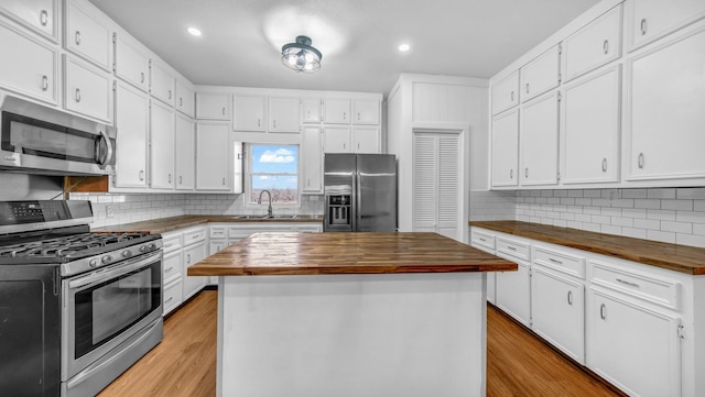 kitchen featuring butcher block counters, stainless steel appliances, white cabinets, and a kitchen island