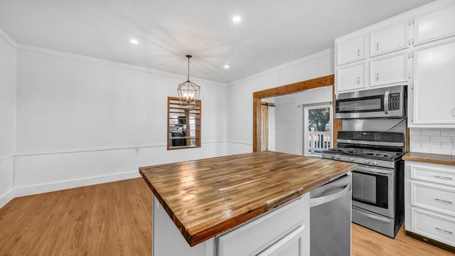 kitchen featuring butcher block counters, white cabinetry, a center island, hanging light fixtures, and appliances with stainless steel finishes