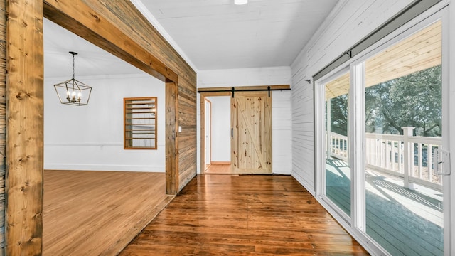 interior space with wood walls, an inviting chandelier, ornamental molding, a barn door, and hardwood / wood-style floors