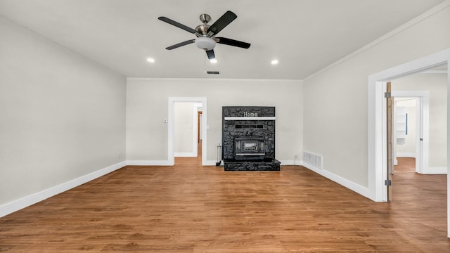 unfurnished living room with ceiling fan, wood-type flooring, a stone fireplace, and ornamental molding