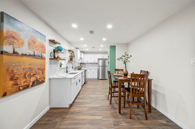 kitchen with sink, appliances with stainless steel finishes, white cabinets, hardwood / wood-style floors, and backsplash