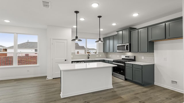 kitchen with a kitchen island, appliances with stainless steel finishes, sink, backsplash, and hanging light fixtures