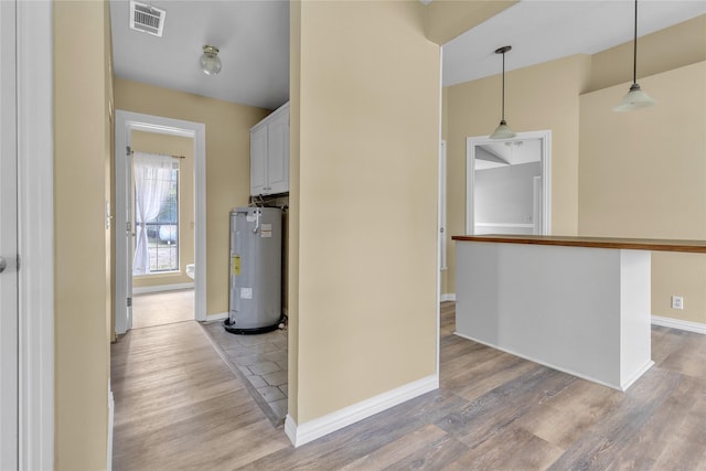 hall with visible vents, baseboards, electric water heater, and light wood-style floors