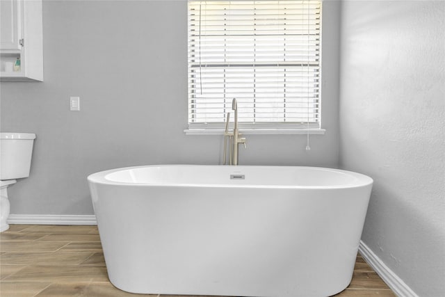 bathroom with wood finish floors, a freestanding bath, and baseboards