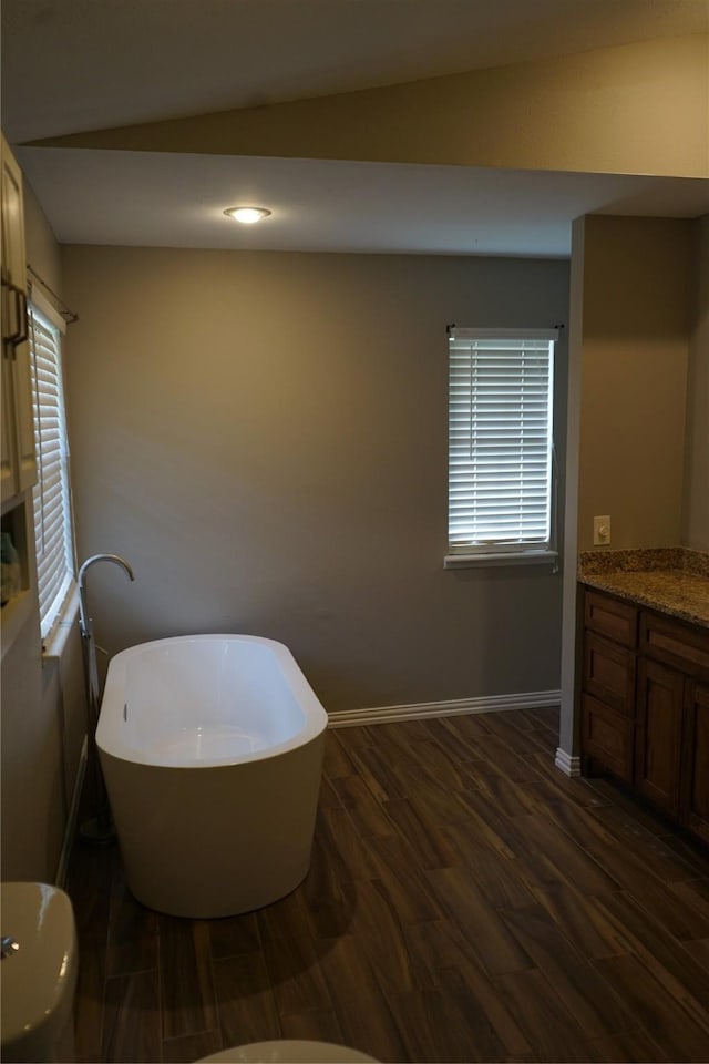 bathroom with a freestanding bath, vanity, baseboards, and wood finished floors