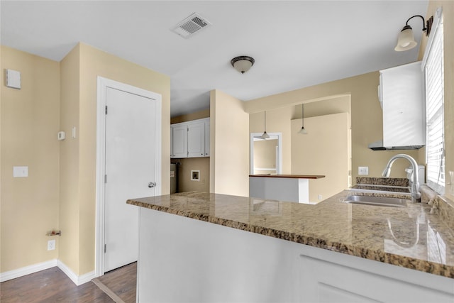 kitchen featuring stone counters, dark wood-type flooring, a sink, visible vents, and baseboards