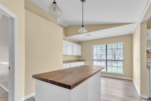 kitchen featuring baseboards, white cabinets, lofted ceiling, butcher block countertops, and decorative light fixtures