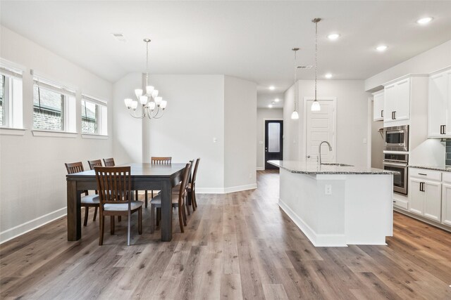 dining room with an inviting chandelier, sink, wood-type flooring, and vaulted ceiling