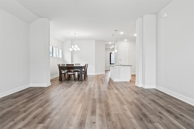 unfurnished dining area featuring a chandelier, recessed lighting, a sink, wood finished floors, and baseboards