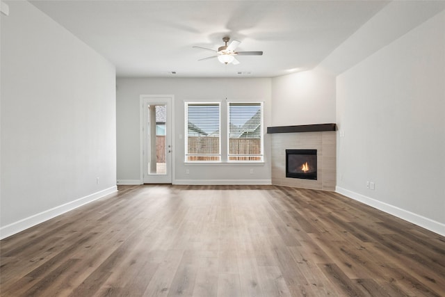 unfurnished living room with a tiled fireplace, dark wood-type flooring, and ceiling fan