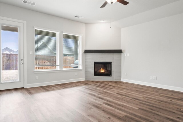 unfurnished living room featuring a tile fireplace, hardwood / wood-style floors, and ceiling fan