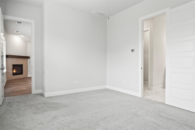 unfurnished room with a lit fireplace, visible vents, and light colored carpet