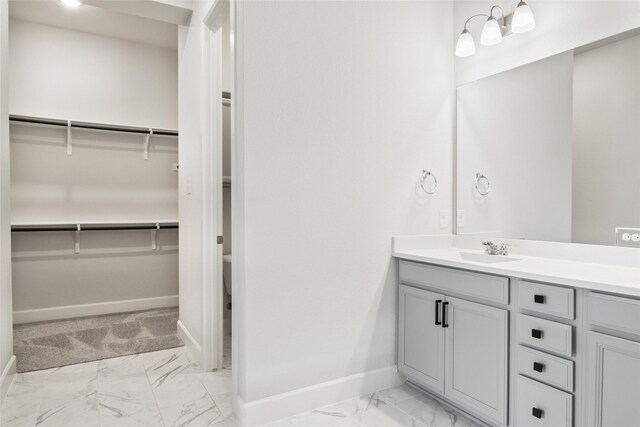 full bath featuring marble finish floor, a spacious closet, baseboards, and vanity