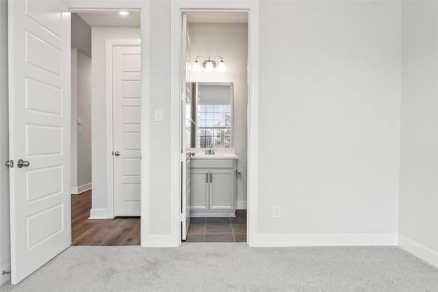 unfurnished bedroom with a sink, dark colored carpet, ensuite bath, and baseboards